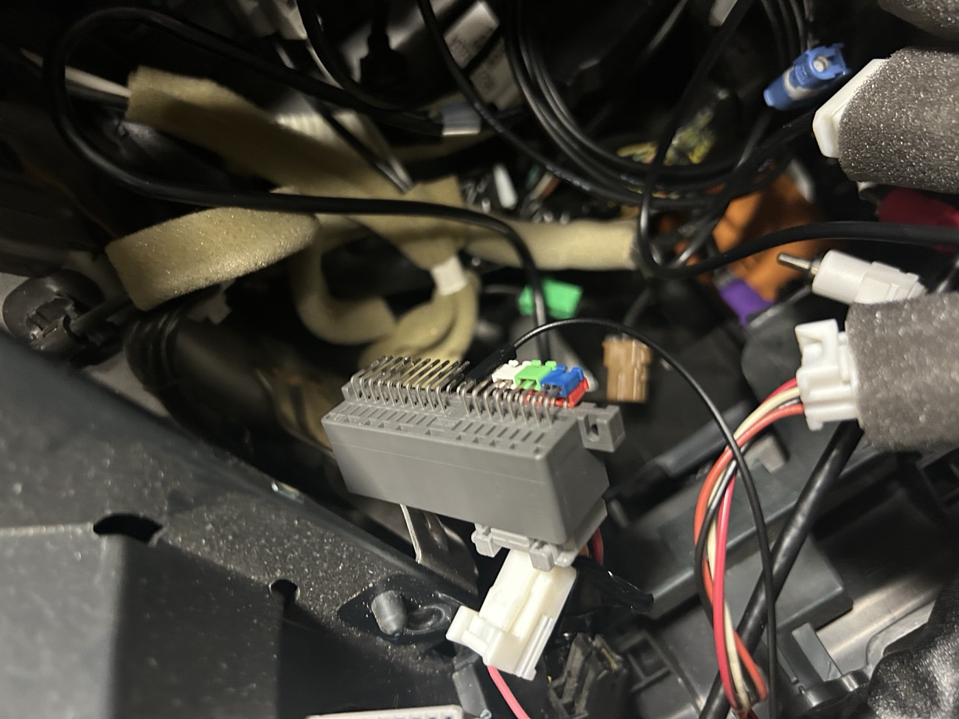 The grey StarLink connector, desoldered from its module, resting among the wiring behind the dash of a Subaru Outback. Its bare pins stand up in two rows.